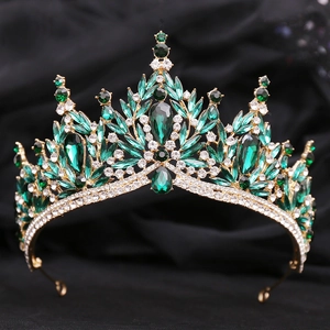 Close-up of luxury bridal crown with emerald crystals and golden leaf details on velvet
