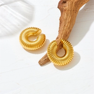 Golden hollow twisted hoop earrings with textured vertical ridges on a wooden branch
