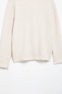 Détail d'un cardigan en fausse fourrure blanc cassé avec texture pelucheuse et ourlet