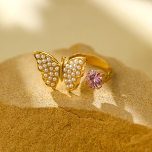 Double-layered gold open ring with pearl butterfly and pink gemstone on a rock