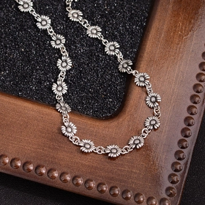 Retro silver daisy necklace featuring linked floral charms on a textured background