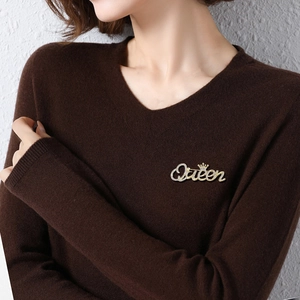 Elegant gold Queen letter brooch with rhinestones and crown pinned on a brown sweater