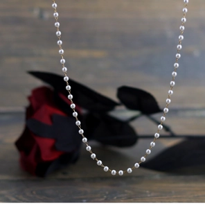 Close-up of elegant small white pearls with a delicate golden chain against dark roses