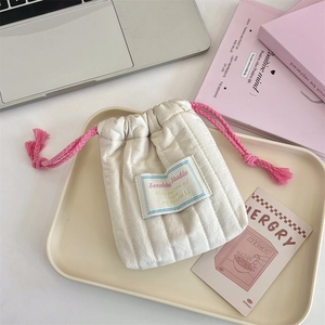 Quilted beige drawstring pouch with pink cords and fabric label on a decorative tray