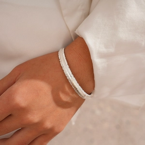 Detailed close-up of a silver textured metal bangle on a wrist with white sleeve