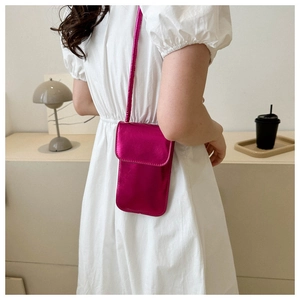 Detail view of a rose pink crossbody phone bag worn by a model in a home setting