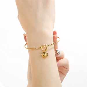 Detailed view of a gold-plated knot bangle with a spherical charm on a female wrist