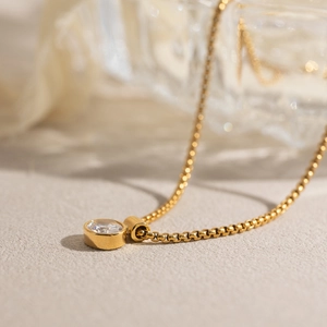 Macro shot of 18K gold box chain necklace with a bezel-set white zircon pendant