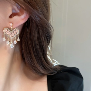 Close-up of golden heart tassel earrings with pink gems and white zircon on a model