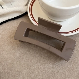 Close-up of a large coffee brown square hollow hair claw clip on beige fabric
