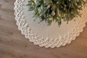 Dettaglio del copribase per albero di Natale in maglia intrecciata crema su parquet