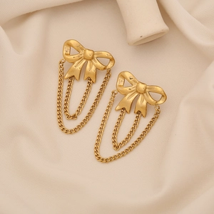 Detail of gold bow earrings featuring layered tassel chains on soft cream fabric
