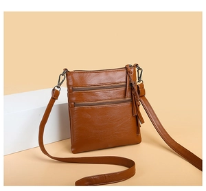 Detail of brown leather crossbody phone bag featuring triple zipper pockets and fringe tassel
