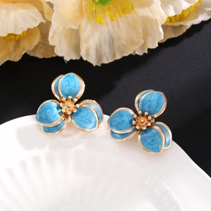 Detailaufnahme blauer Emaille-Blumenohrringe mit Goldrand auf einer Keramikschale