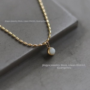 Macro shot of 18K gold plated beaded chain with a round white jadeite pendant on stone