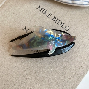 Macro detail of a dolphin-shaped hair claw with marbled acetate and crystal accents