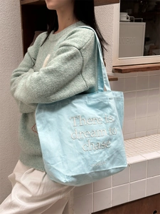 Minimalist light blue canvas tote bag with white embroidery for women on a shoulder