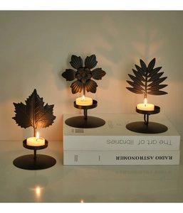 Detail of three black metal leaf-shaped tea light holders on a white book display