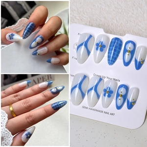 Detail of semi-handmade almond press-on nails with blue floral patterns and gold beads