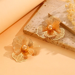 Detail of hollowed flower earrings in gold finish resting on a marble surface