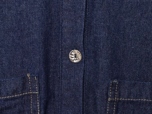 Detailed close-up of dark blue denim shirt with silver metal button and orange stitching