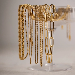 Detail of multiple layered gold plated necklaces with paperclip and twist chains on glass