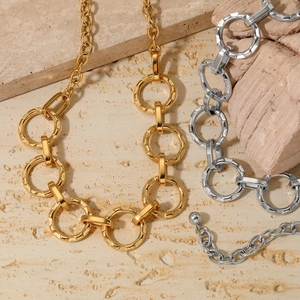 Flat lay of chunky gold and silver chain necklaces on stone and wood elements