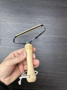Close-up of manual lint remover with wooden handle and copper metal head on dark wood table