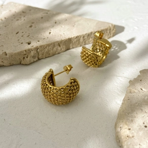 Detailed view of gold C-shaped earrings with textured dots on a natural stone background