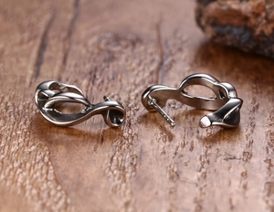 Detailed close-up of punk style sword stud earrings for men on a dark wood surface