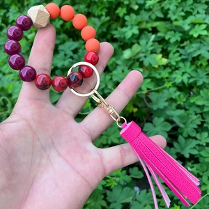 Detail eines Perlen-Schlüsselanhänger-Armbands mit lila Perlen und pinker Lederquaste