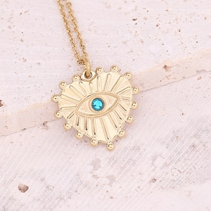 Close-up of golden evil eye heart pendant with blue gemstone on a textured stone