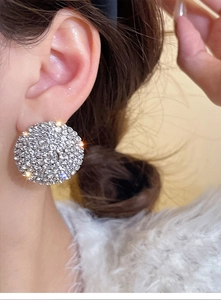 Close-up of oversized silver round earrings with shimmering rhinestones worn by a model