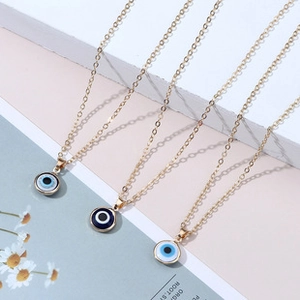 Three gold layered cross necklaces featuring blue evil eye pendants on a textured surface