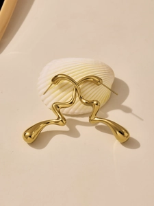 Vue détaillée des boucles d'oreilles gouttes dorées 18k en acier poli sur un coquillage