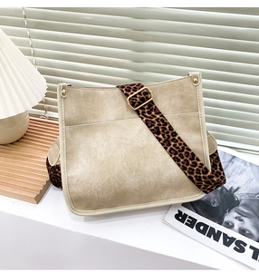 Detail of minimalist beige tote bag featuring a wide leopard print strap and golden buckle