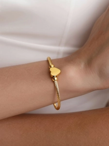 Detail of 18k gold heart bangle showing twisted rope texture on a model's wrist
