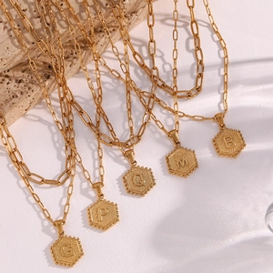 Detailed view of golden paperclip chain necklaces with hexagonal initial letter pendants