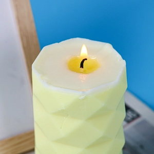 Close-up of a burning yellow geometric faceted pillar candle with diamond pattern