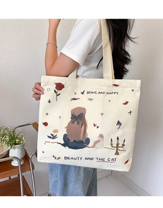 Off-white canvas tote bag featuring cat illustration worn over shoulder for daily use