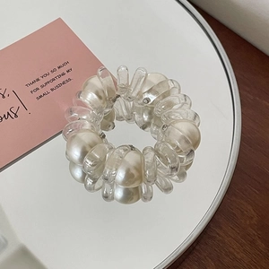 Détail d'un élastique spirale transparent avec perles blanches sur une surface miroir