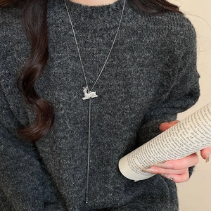 Close-up of silver reindeer pendant necklace with diamonds on a grey knit sweater