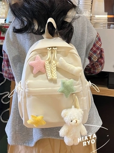 Detail of cream canvas backpack with plush stars and bear charm on back of person