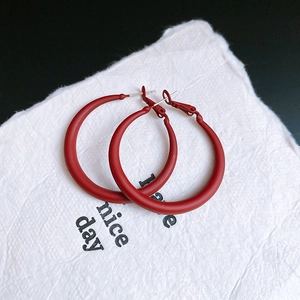 Macro shot of large matte red C-shaped hoop earrings on white textured paper background