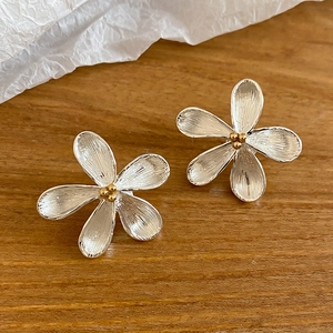 Dettaglio di orecchini a fiore in metallo spazzolato argento con centro dorato