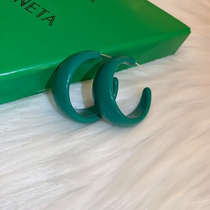 Macro shot of green resin C-shape hoop earrings on a soft white plush surface