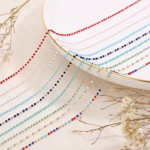 Detailed close-up of colorful enamel beaded chains in various hues on a white ceramic plate