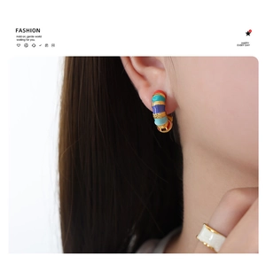 Close-up of a model wearing colorful enamel striped hoop earrings in a retro gold finish
