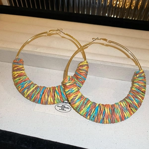 Detailed close-up of large golden hoop earrings with colorful bohemian woven texture details