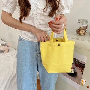 Minimalist yellow canvas lunch bag shown in lifestyle setting with metal fastener